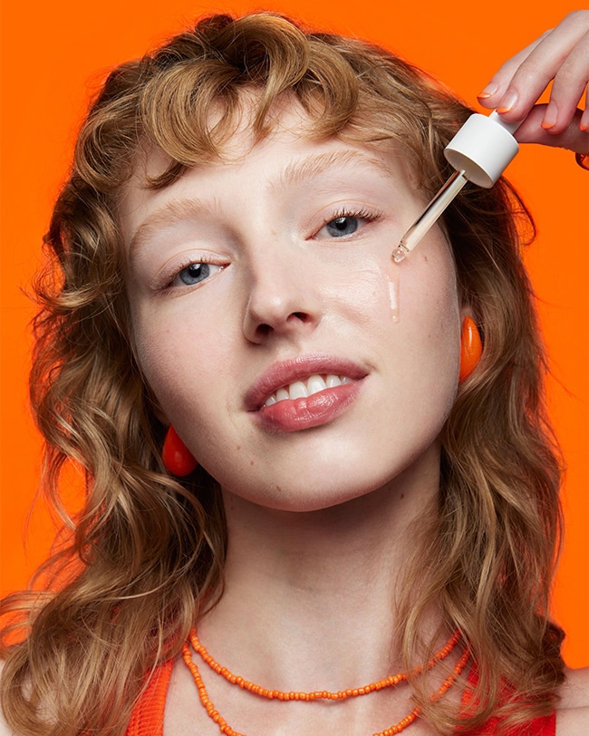 Woman applies vitamin c serum to skin with serum dropper applicator. 