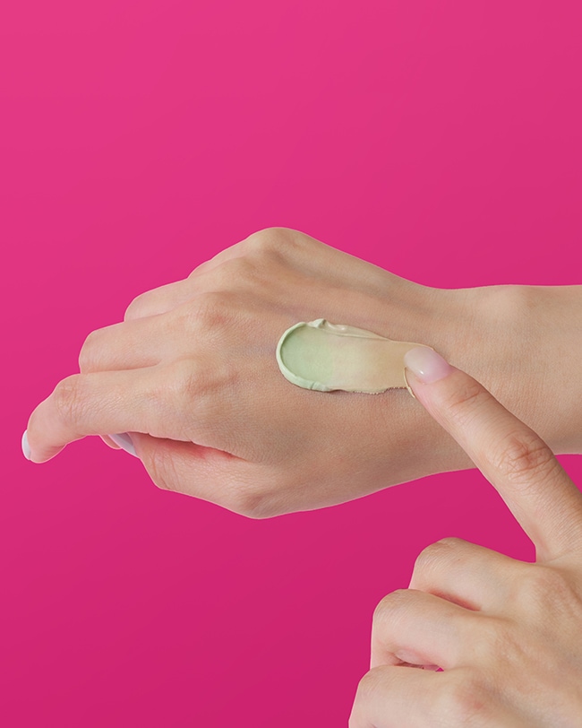 Woman smiles with dollops of Cicapair moisturizer cream applied to her cheeks and chin.