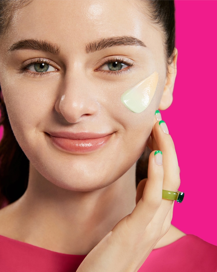 Woman with swipe of Cicapair color corrector on cheek. Texture of color corrector swatch is transitioning from green to beige.