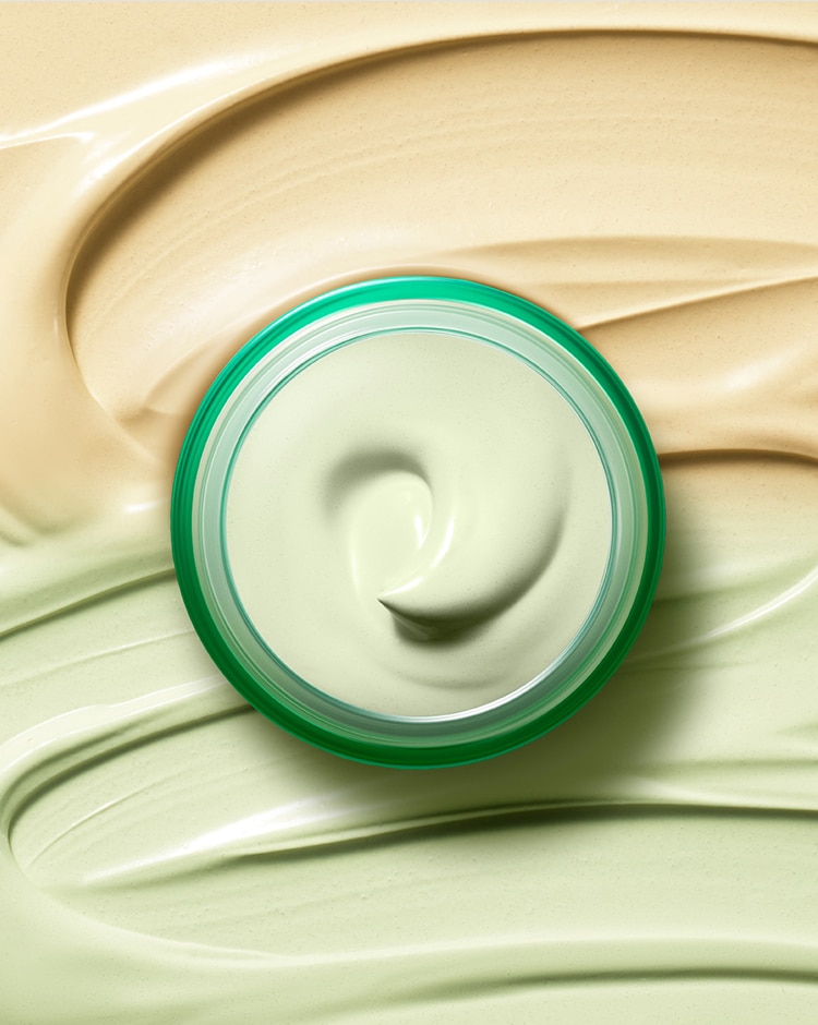 Open jar of Cicapair Color Correcting Treatment reveals smooth green formula. Jar is positioned on cream texture. 