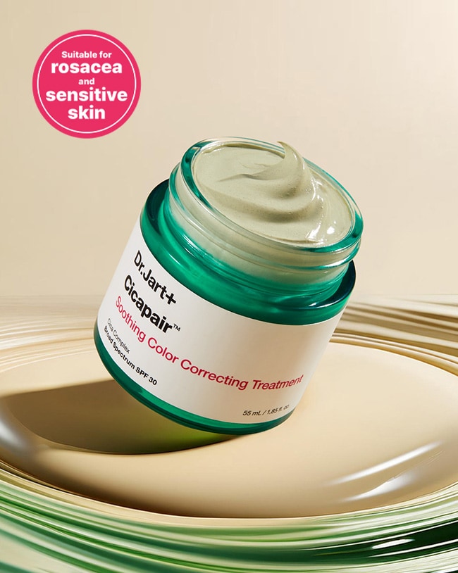 Jar of color corrector is tilted and open showing creamy texture on a beige background. 