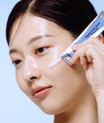 A model smiles while applying pumps of cleanser to her cheek area 