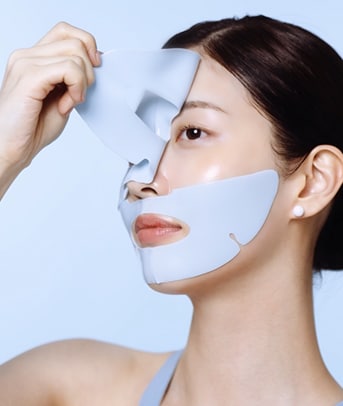 A model smiles while applying pumps of cleanser to her cheek area.