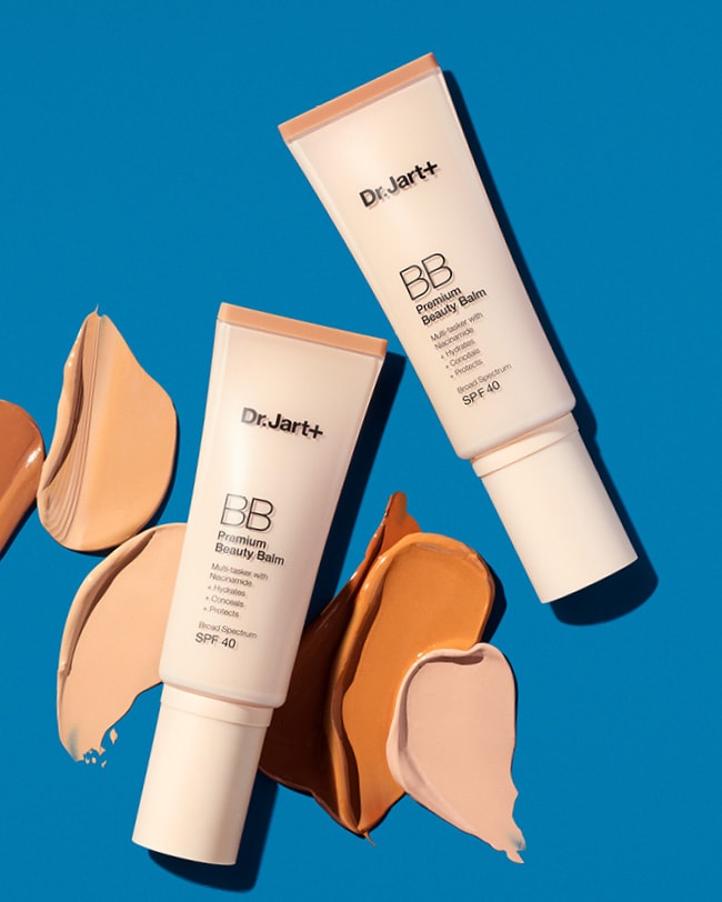 Two bottles of Premium BB Tinted Moisturizer are on a dark background showcasing the shade range thru the textures.