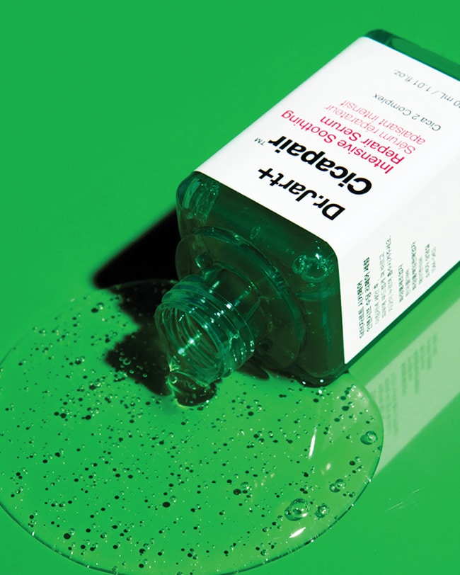An open bottle of Cicapair Serum is displayed with the contents pouring out of the bottle showing the texture. 