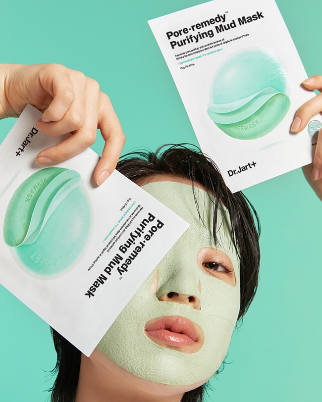Model is holding two packages Pore remedy™ Purifying Mud Face Mask while wearing a mask on her face. 