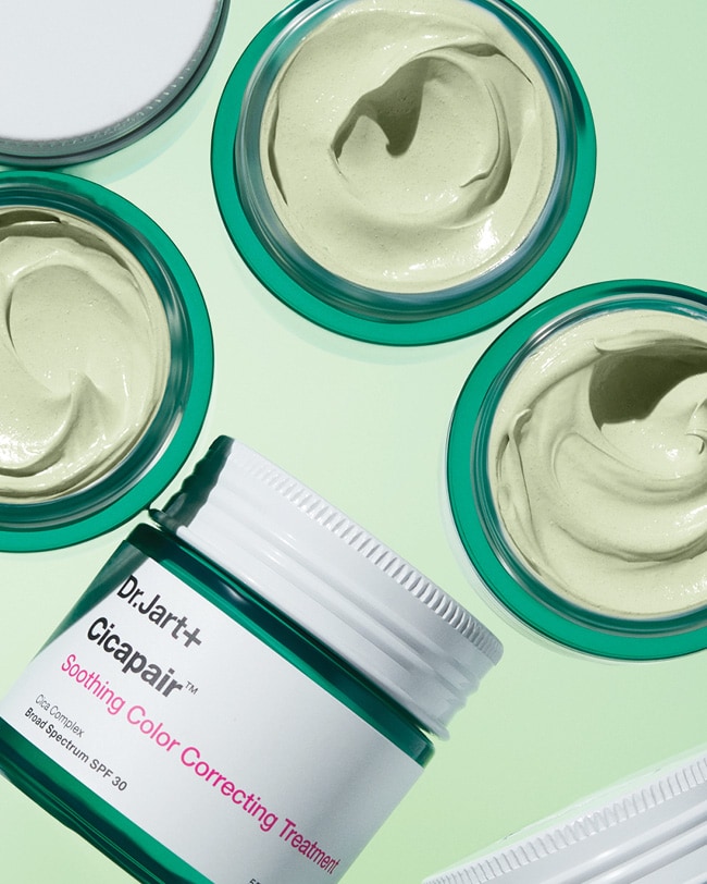 Jars of Cicapair color corrector, some opened and some closed, are displayed on a light green background. 