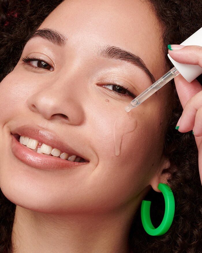 Woman applies Cicapair Serum liquid to cheek; close up of serum eyedropper applicator.
