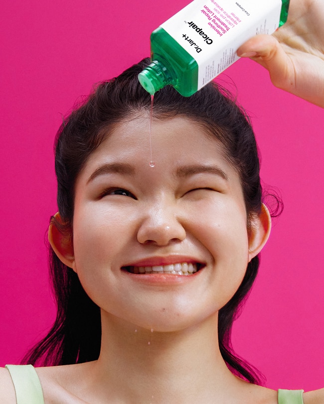 Woman pours out a drop of Cicapair Liquid Lotion Toner from bottle.